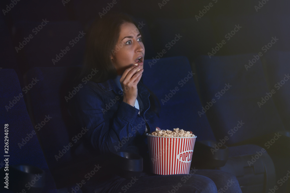 Fototapeta premium Young woman watching movie and eating popcorn in cinema