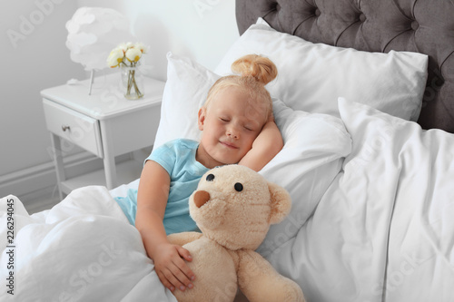 Cute little girl with teddy bear sleeping in bed