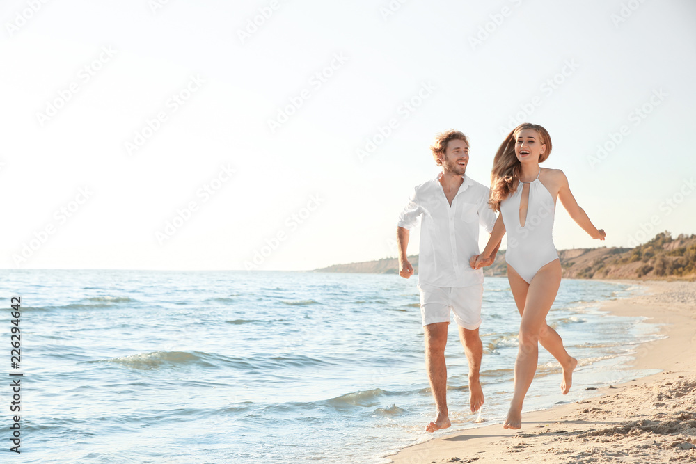 Happy young couple in beachwear running together on seashore. Space for text
