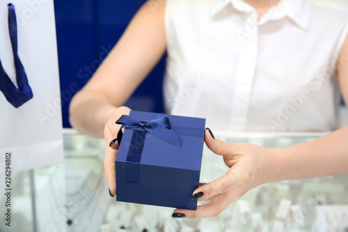 Young shop assistant with gift box and bag in jewelry store photo