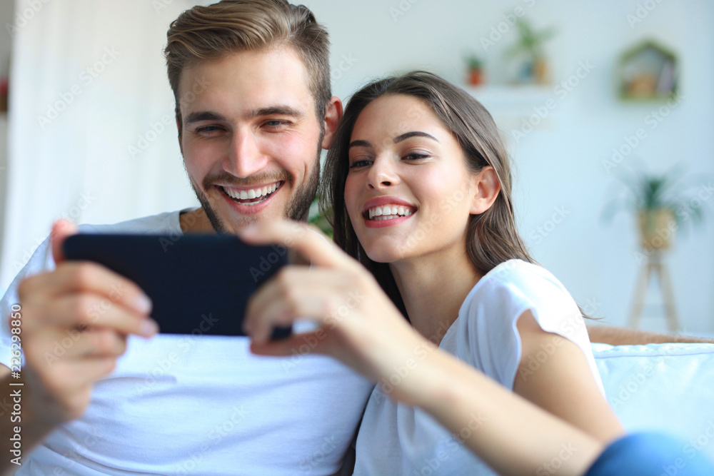 Young couple watching online content in a smart phone sitting on a sofa at home in the living room. Young couple watching online content in a smart phone sitting on a sofa at home in the living room.