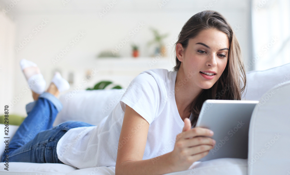Beautiful young woman using tablet sitting on sofa at home at living room. Beautiful young woman using tablet sitting on sofa at home at living room.
