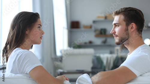 Billede på lærred Side view of a couple talking sitting on a couch and looking each other at home
