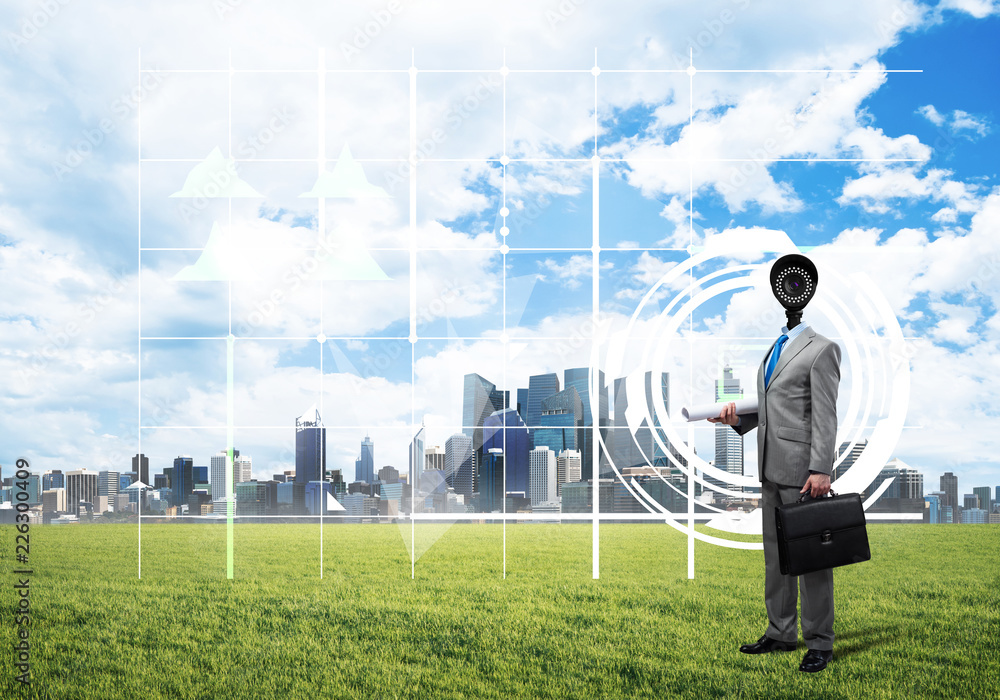 Camera headed man standing on green grass against modern cityscape Camera headed man standing on green grass against modern cityscape