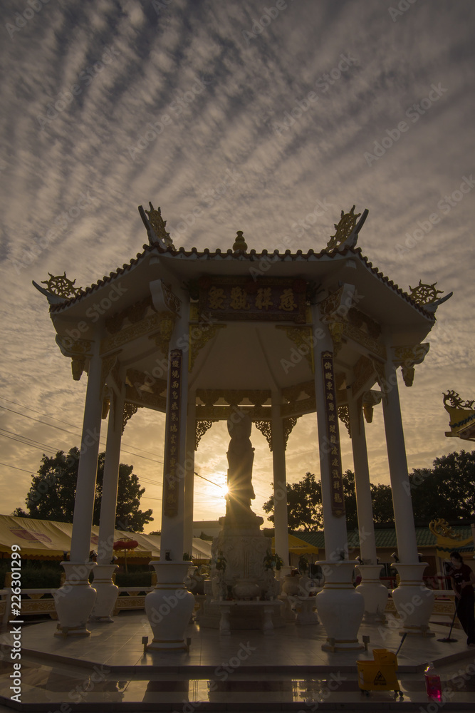 Phuket Thailand - 11 August 2018 - Statue of Guan yin or Kuan im, chinese god in octagon pavilion with yellow sunlight beam and Cirrocumulus cloudy sky background