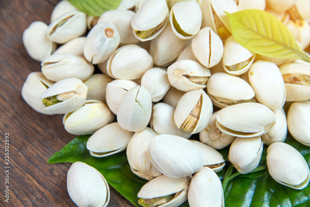 Close up of Pistachios nuts on wooden table. Pistachio in wooden bowl in background with green leaves Close up of Pistachios nuts on wooden table. Pistachio in wooden bowl in background with green leaves