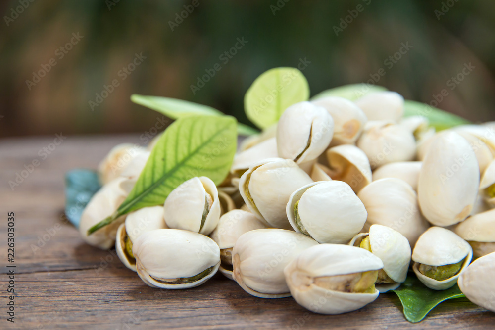 Close up of Pistachios nuts on wooden table. Pistachio in wooden bowl in background with green leaves Close up of Pistachios nuts on wooden table. Pistachio in wooden bowl in background with green leaves