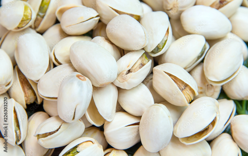 Close up of Pistachios nuts on wooden table. Pistachio in wooden bowl in background with green leaves Close up of Pistachios nuts on wooden table. Pistachio in wooden bowl in background with green leaves