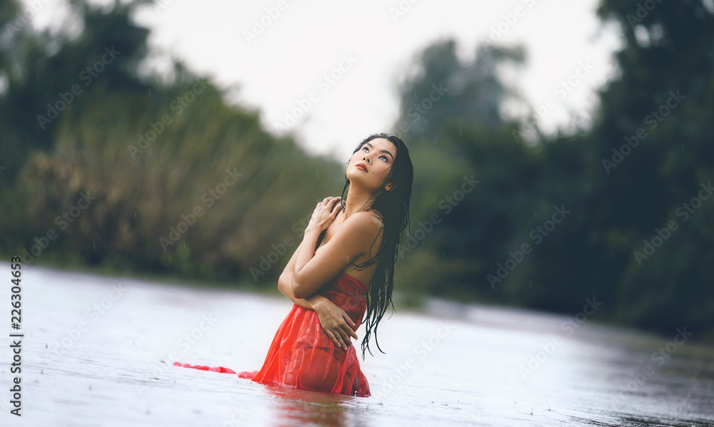 An Asian woman in red bathrobe is enjoying rain and nature in the wild. - obrazy, fototapety, plakaty 