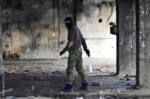 Masked man with machete, in ruined building.