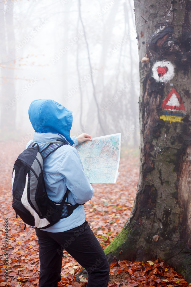 Young woman looking at the map while hiking through a forest on a foggy autumn day