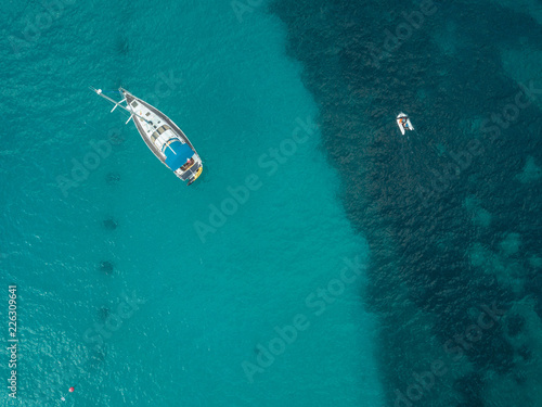 Aerial bird's eye view drone of boat docked in mediterranean tropical beach with turquoise - sapphire waters