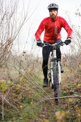 Determined young bearded man riding mountain bike through bushes on a cold foggy autumn or winter day
