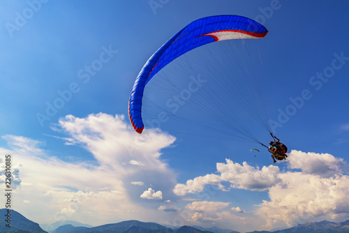 2018-08-23, Saint-Vincent-les-Forts, France. Tandem paragliders fly with beautiful clouds on the background.