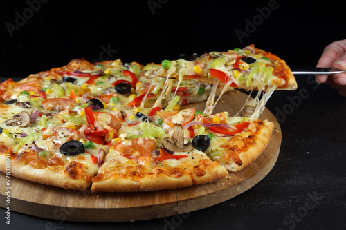 Vegetarian multicolored pizza, cut into pieces, one of which is pulled with a spatula