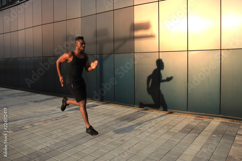 Full length of young African man in sports clothing jogging while exercising outdoors  at sunset or sunrise. Runner.