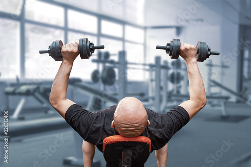 The bald man presses dumbbells from a breast.