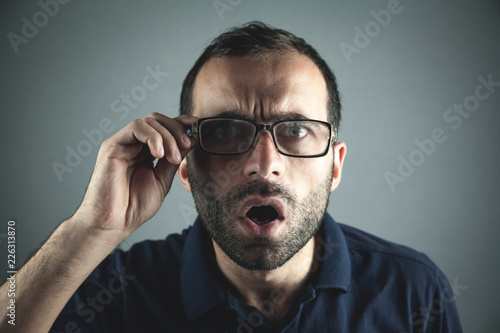 Shocked man fixing eyeglasses and looking at camera.
