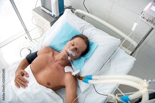 Serious disease. Top view portrait of male patient on mechanical ventilator resting in recovery room photo