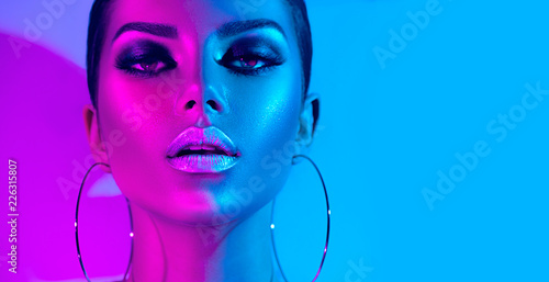Fashion model brunette woman in colorful bright neon lights posing in studio. Beautiful sexy girl, trendy glowing makeup, metallic silver lips