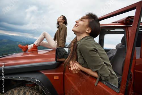 Cheerful beautiful young woman enjoying her active weekend with her friend while traveling in the off-road car