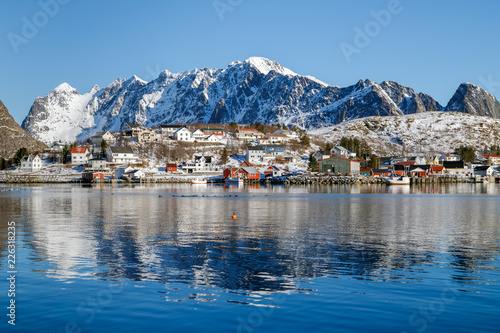 Beautiful winter landscape on Lofoten islands with traditional fishing village, red rorbu houses and mountains in the background. Reflection on water. Travel Norway.