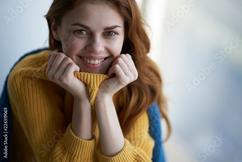 happy woman in yellow sweater sits near the window