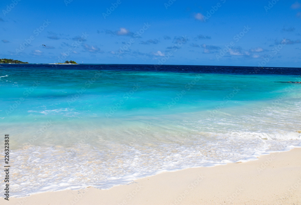 A seascape of pristine beach and deep blue ocean, on a tropical island, in the Maldives.