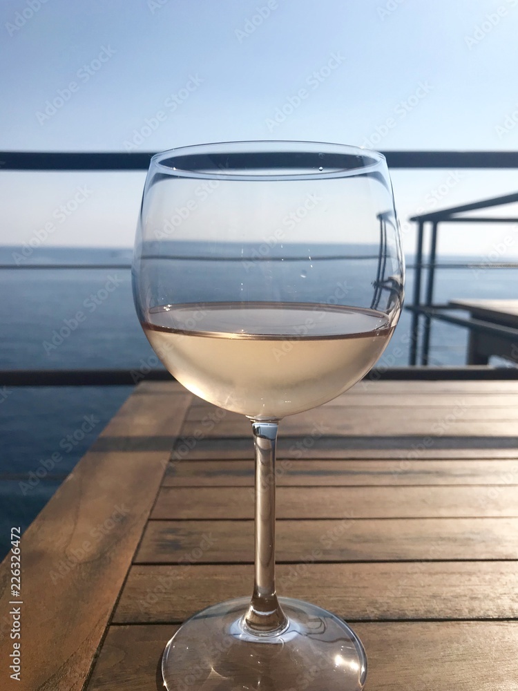 Glass of Rose wine sitting on a wooden table with the sea in the background, taken on a summer's day in Italy. 