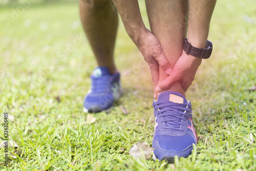 sportman holding his ankle pain while jogging or run in national park.