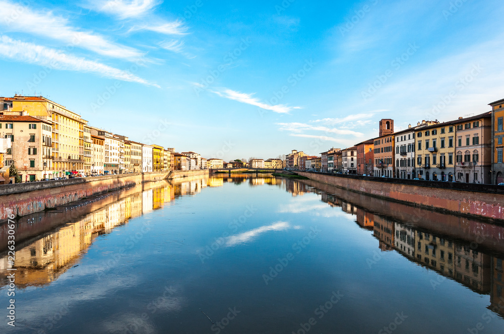 Beautiful river in the central part of Pisa surrounded with small houses reflecting in the water with blue sky on the background