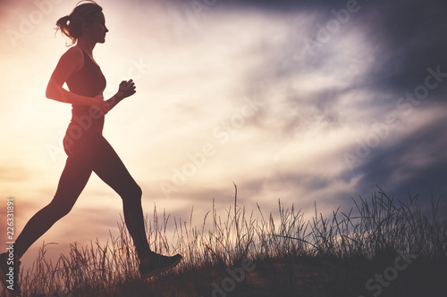Young woman running on the field near seaside at sunset. Active person outdoors at the dusk in summer