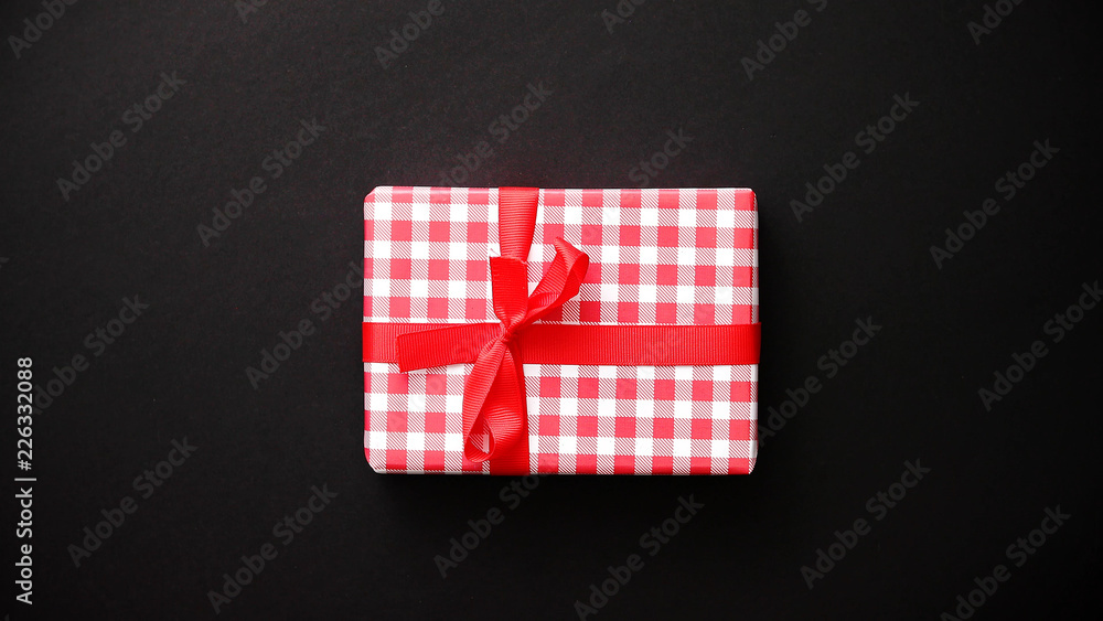 Gift box wrapped with red checkered pattern christmas paper with red bow on black table, top view