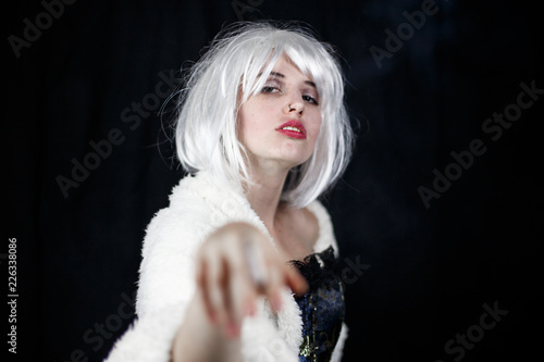 Fototapeta Naklejka Na Ścianę i Meble -  Attractive young woman in costume smoking cigar and looking at camera while standing on black background 