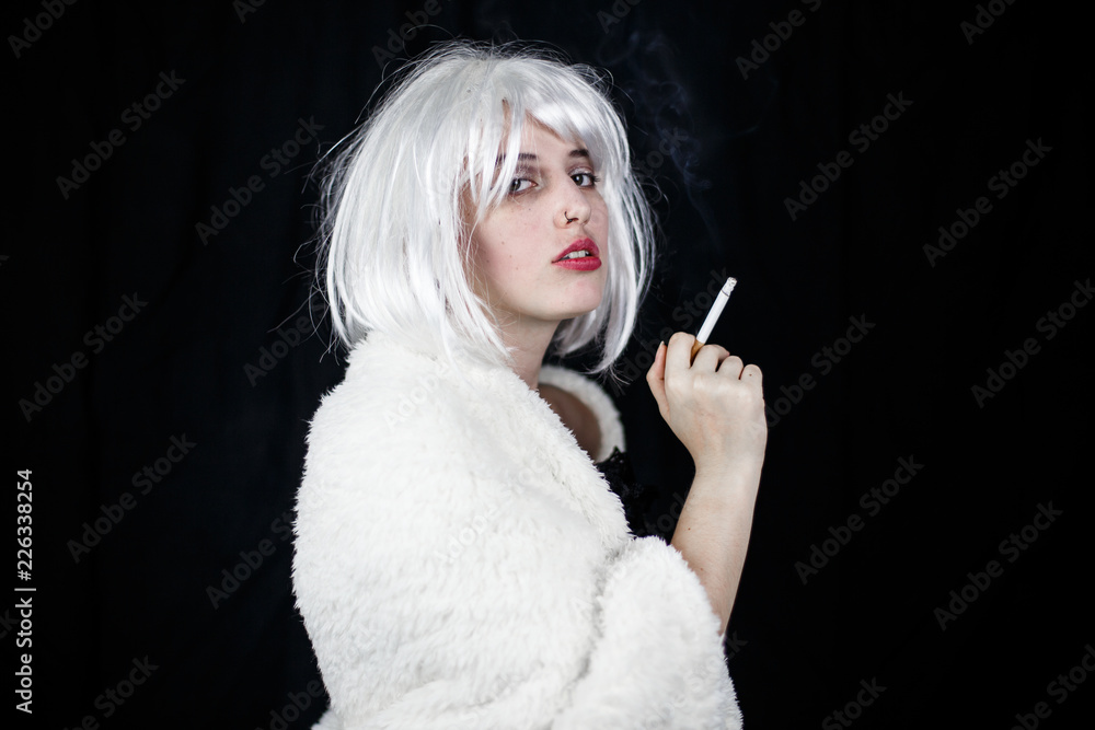 Obraz premium Attractive young woman in costume smoking cigar and looking at camera while standing on black background 