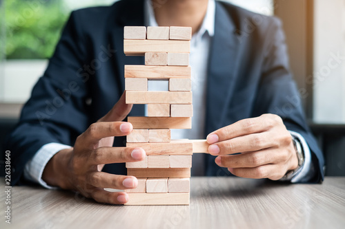 Businessman hand placing or pulling wooden block on the tower. Business planning, Risk Management, Solution and strategy Concepts photo
