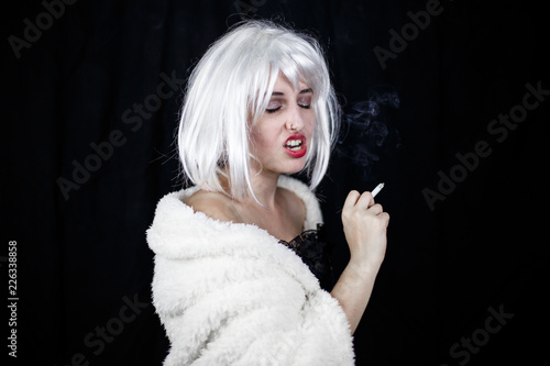 Fototapeta Naklejka Na Ścianę i Meble -  Attractive young woman in costume smoking cigar and looking at camera while standing on black background 