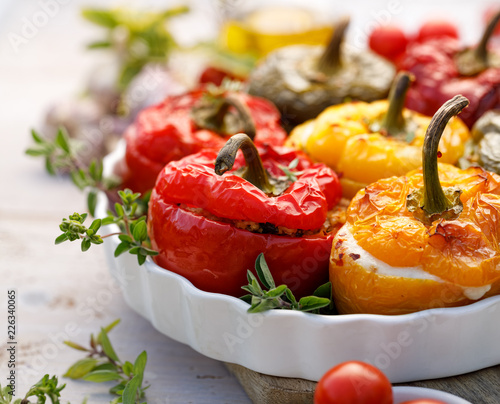 Roasted bell pepper with mushroom, rice, cheese and herbs filling in a baking dish on a white wooden table, close-up. A healthy and delicious vegetarian food.