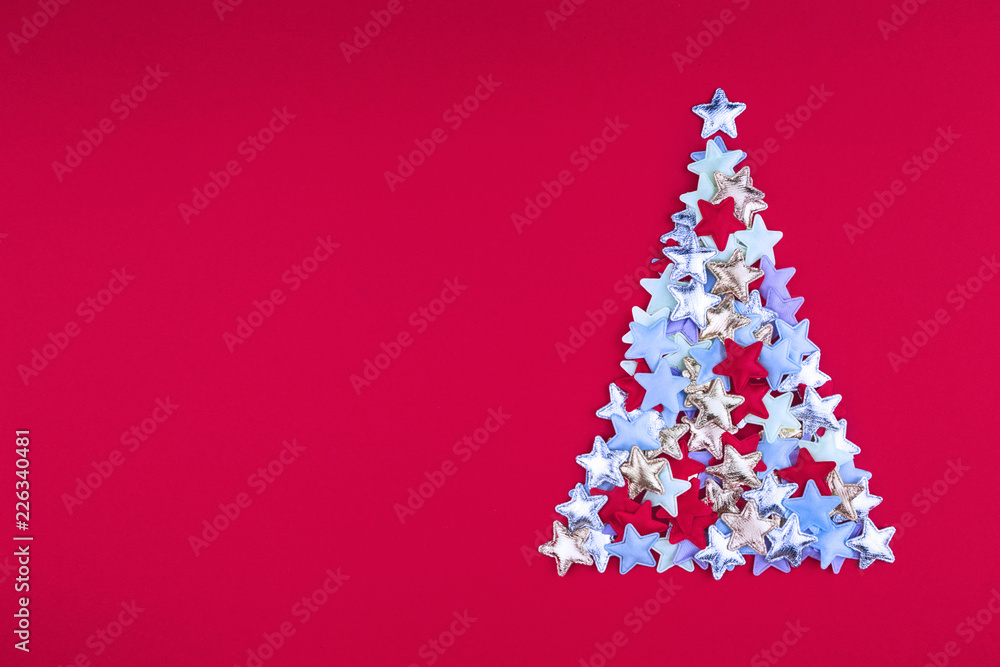 Christmas tree of colored small stars on bright red background in flat lay style Christmas tree of colored small stars on bright red background in flat lay style