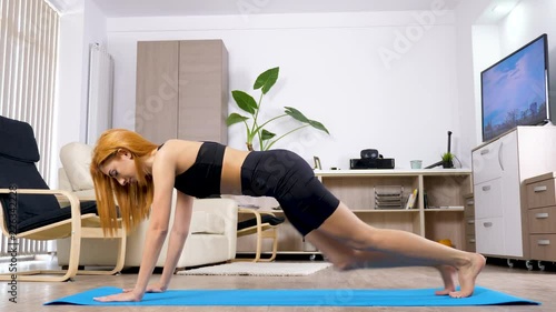 Woman does sport at home. She is doing exercises for legs muscle on a blue mat in linving room of her home. She is a beautiful arabian mixed race young woman. Dolly slider 4K footage photo