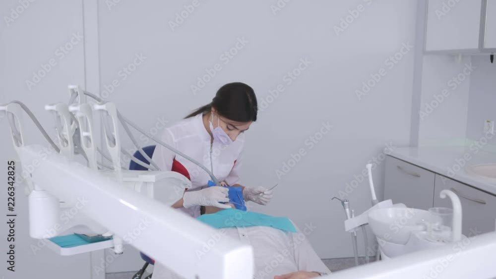 Dentist is treating patient in modern dental office. The operation is carried out using cofferdam. Dentist is treating patient in modern dental office. The operation is carried out using cofferdam.