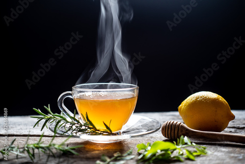 Hot tea in glass cup with steam and lemon .tea leaves and mint herb on wood background