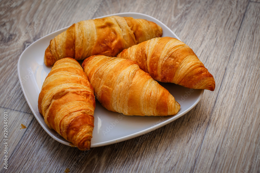 Delicious croissants on a square white plate on a wooden tabletop.