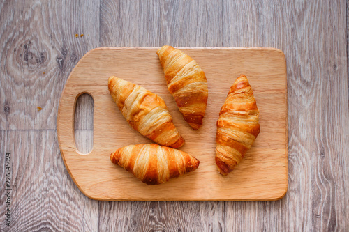 Four croissants on a wooden light cutting board on a wooden tabletop.
