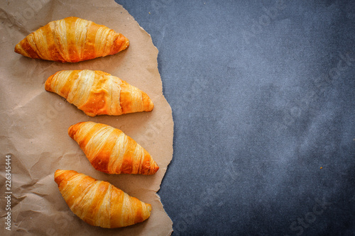 Four croissants on brown craft paper on a dark contrasting background.