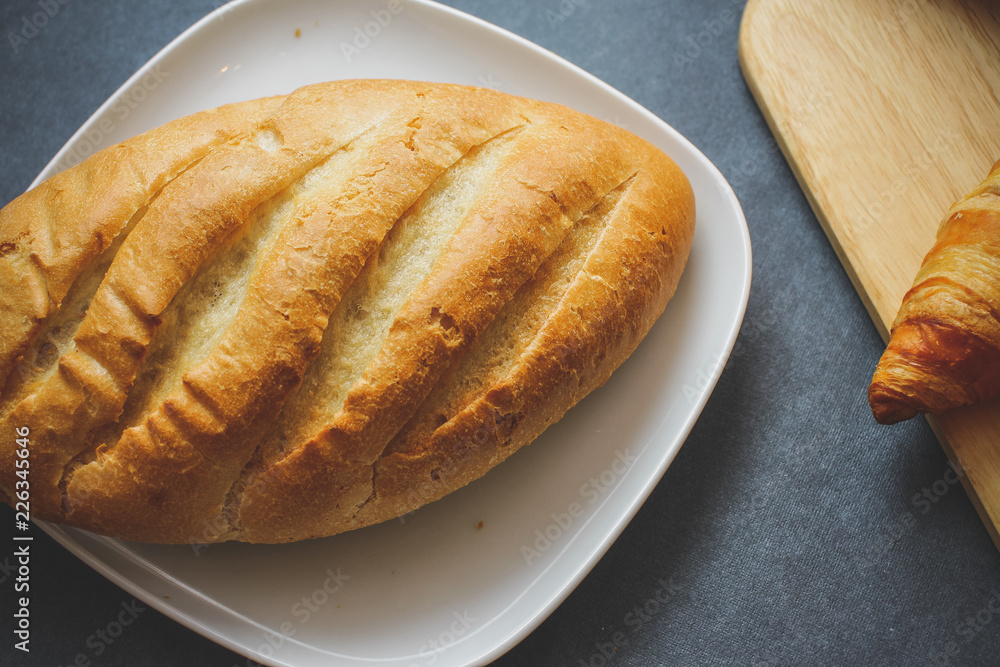 French loaf and four croissants on a wooden cutting board on dark craft paper. French loaf and four croissants on a wooden cutting board on dark craft paper.