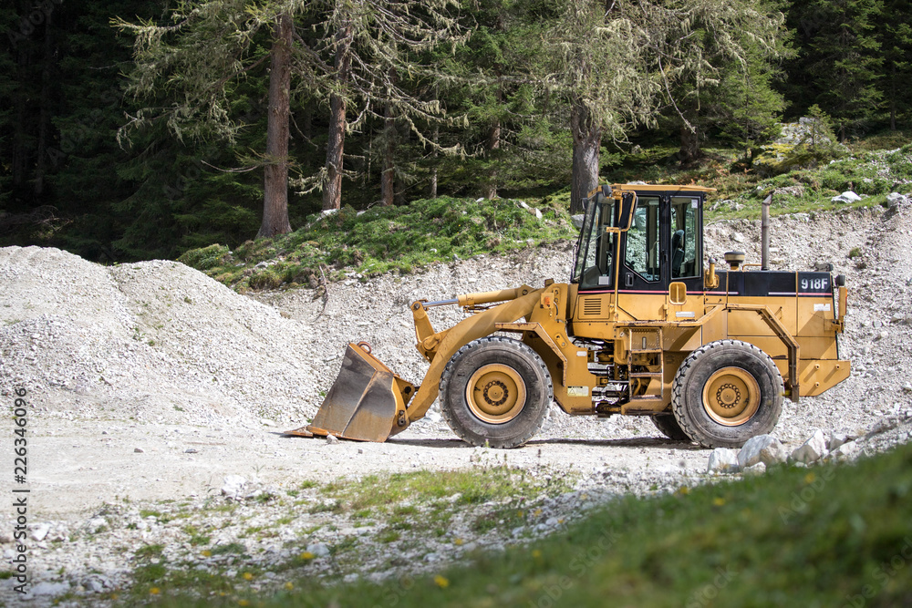 Bagger auf Baustelle, Schottergrube und Bäume im Hintergrund Bagger auf Baustelle, Schottergrube und Bäume im Hintergrund