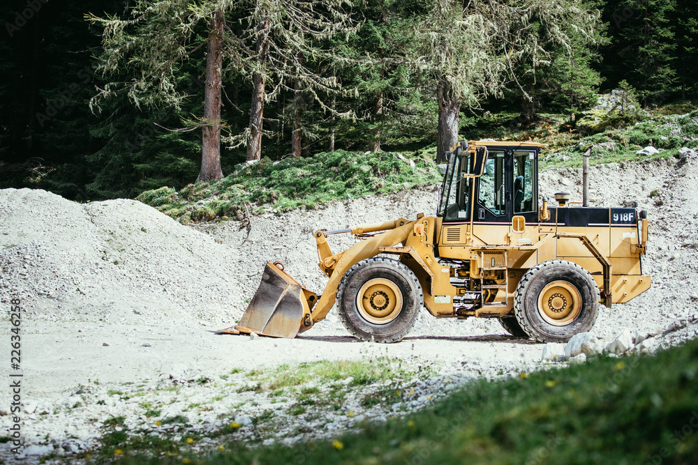 Bagger auf Baustelle, Schottergrube und Bäume im Hintergrund Bagger auf Baustelle, Schottergrube und Bäume im Hintergrund