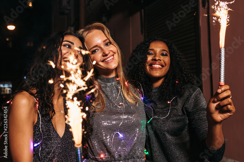Young girls walking outdoors with sparklers and christmas lights around their bodies