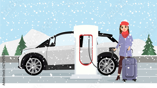 Woman charges an electric car at a charging station for electric vehicles. Winter time. Snow.